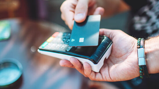 Adult man paying with credit card at cafe, close-up of hands with credit card and credit card reader