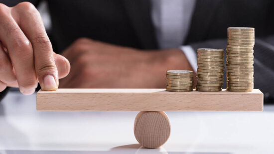 Businessperson Balancing Stacked Coins On Wooden Seesaw